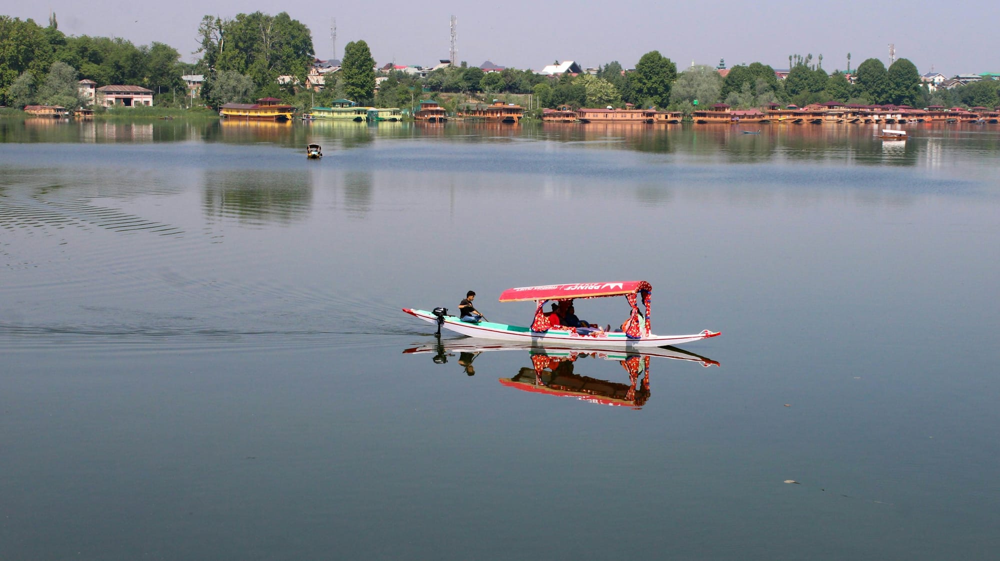 A shikara with a red canopy gliding across a still Dal Lake in Srinagar